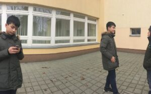 Ein bearbeitets Foto mit einem Jungen in zwei verschiedenen Positionen auf einem Platz. Auf der rechten Seite spricht mit einem anderen Jungen. Auf der linken Seite tippt er mit dem Handy