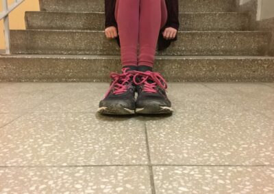 Ein Mädchen sitzt auf den Treppen. Im Vordergrund stehen Schuche durch eine optische Täuschung sehen sie jedoch größer aus.