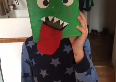 Ein Kind bedeckt sein Gesicht mit einem handgefertigten Dinosauriermaske.