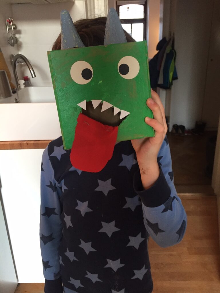 Ein Kind bedeckt sein Gesicht mit einem handgefertigten Dinosauriermaske.