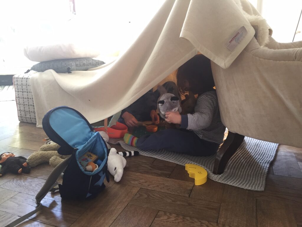 Zwei Kinder sitzen in einem selbstgemacten Zelt im Wohnzimmer.