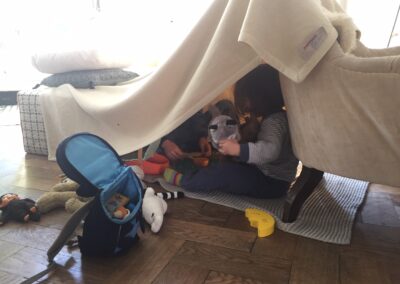 Zwei Kinder sitzen in einem selbstgemacten Zelt im Wohnzimmer.