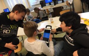 Fünf Kinder sitzen am Tisch und drei von denen schauen in einen Tablet rein