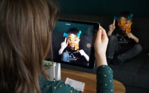 Ein Mädchen nimmt mit einem Tablet ein Video von einem kleinen Jungen auf. Er trägt eine Gesichtsmaske.