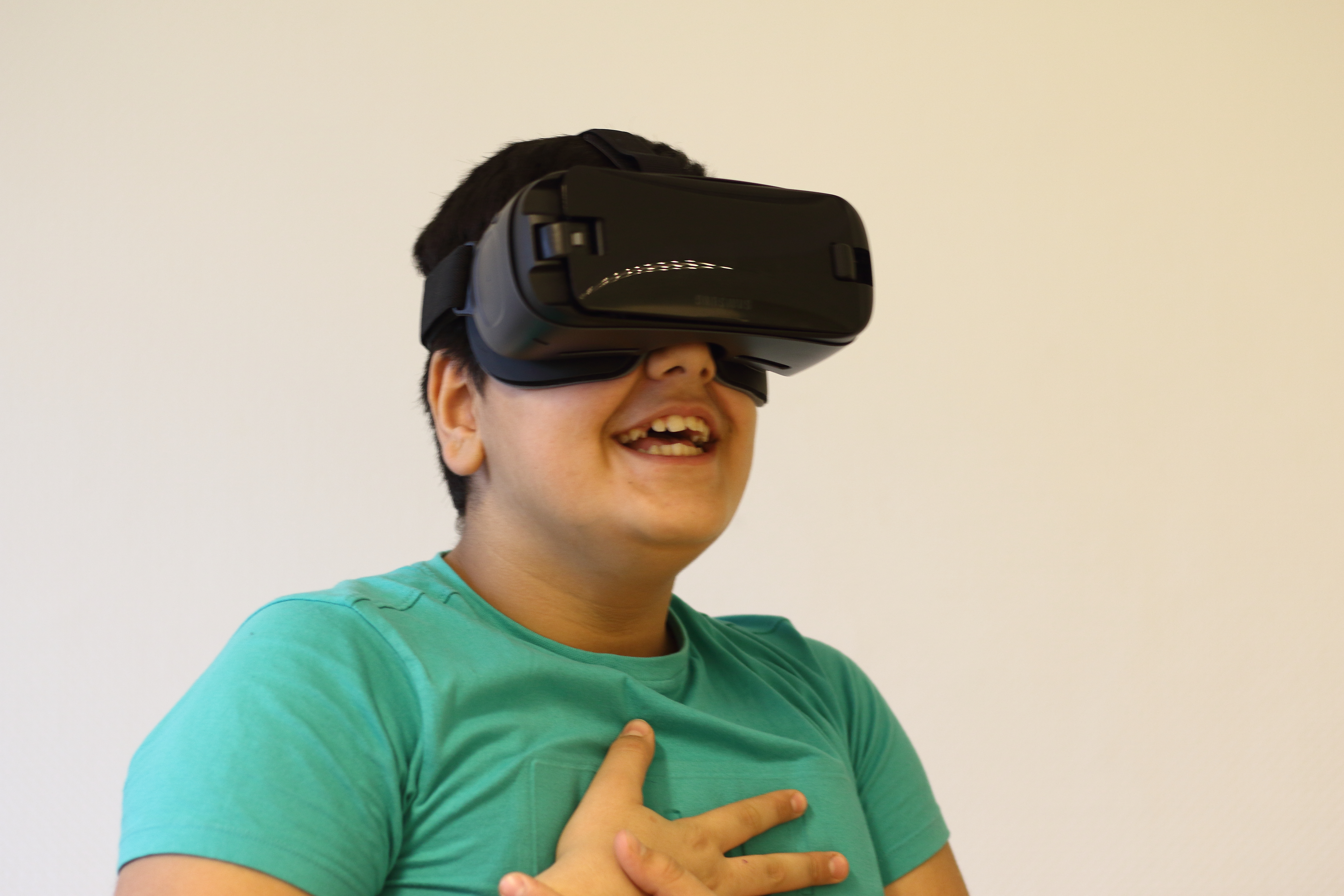 Ein Junge trägt eine Virtual-Reality-Brille und er lacht dabei.