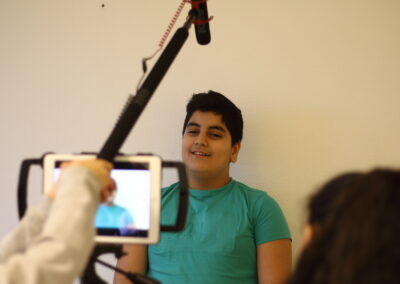Ein Junge steht vor einem Tablet und einem Mikrofon und er wird fotografiert beziehungsweis wird ein Video von ihm aufgenommen