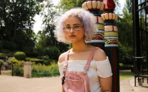 Ein Mädchen steht in einem Park. Sie hat zwei gemalte rote Herzen im Gesicht