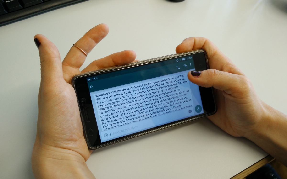 Ein Smartphone-Display von einer Whatsapp Kettenbrief Nachricht wird in der Hand gehalten.