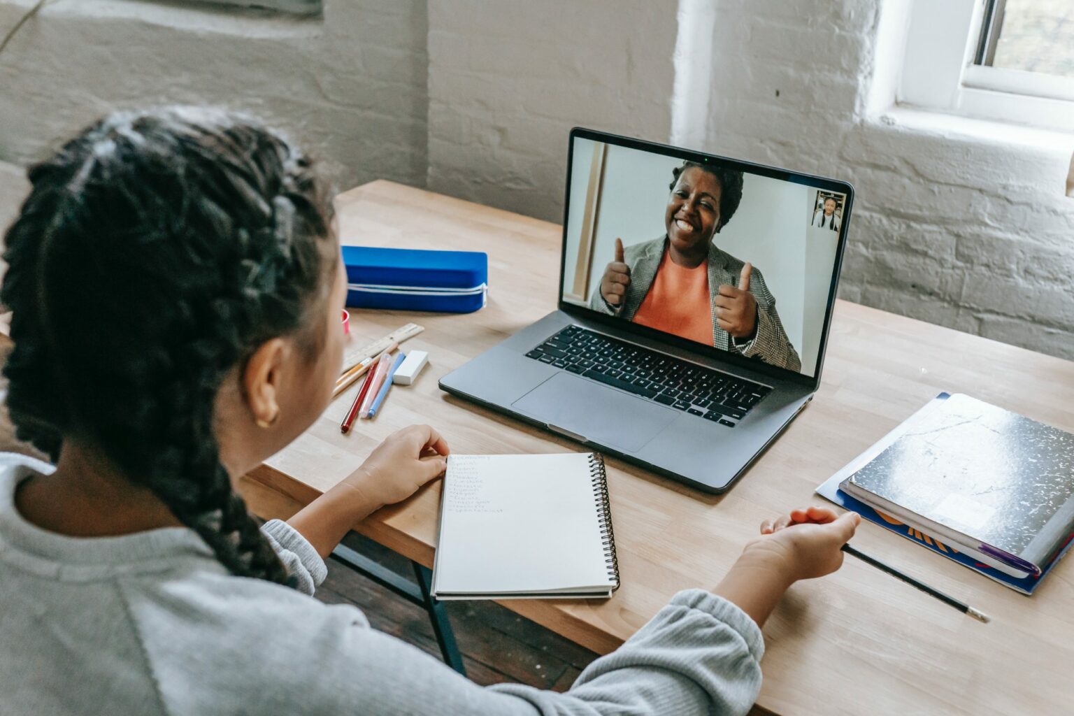 Ein Schulmädchen sitzt an ihrem Arbeitsplatz vor einem Notebook. Sie führt ein Videogespräch mit einer älteren Frau.