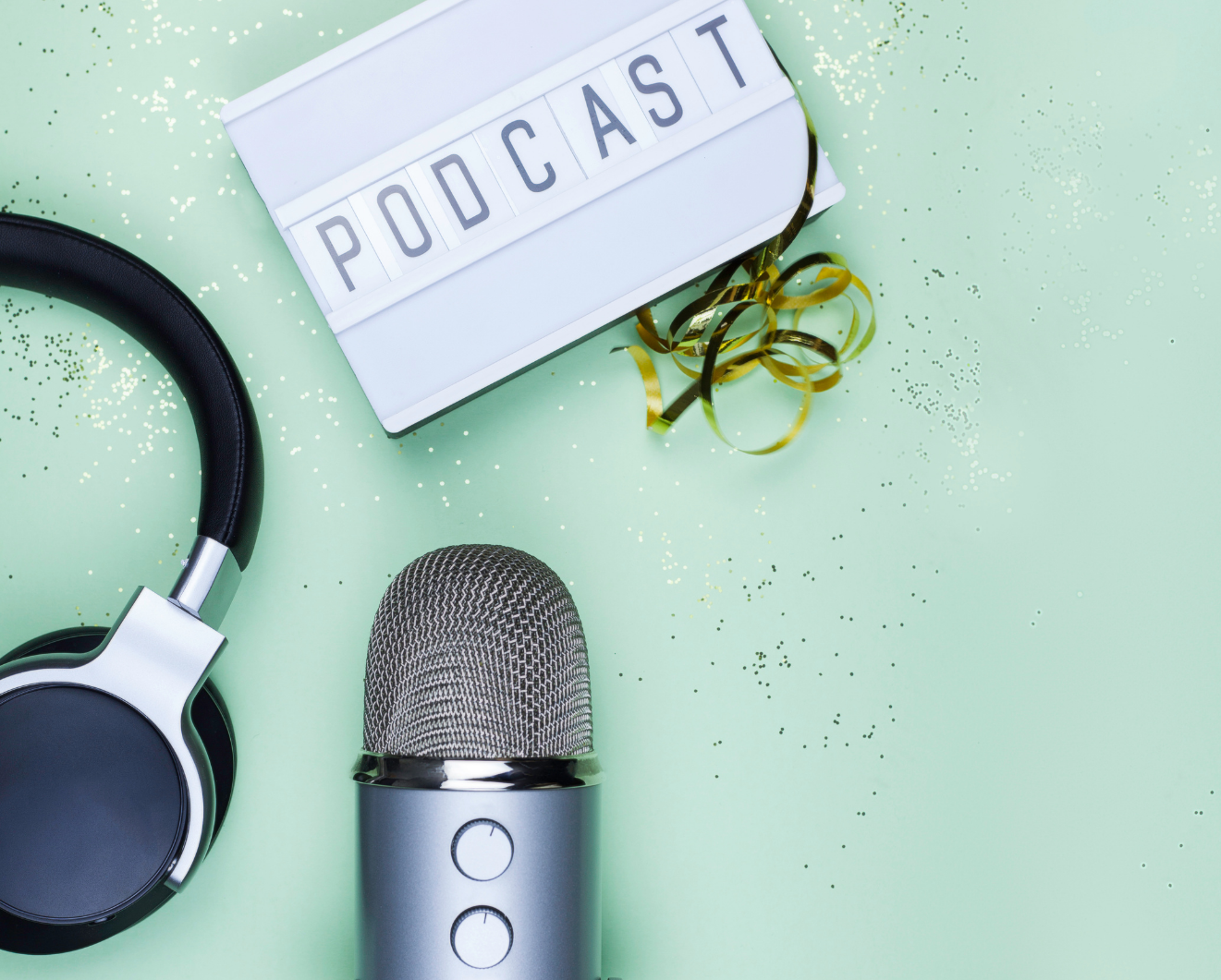 Ein Mikrofon, ein Kopfhörer und ein Schild, mit dem Wort "Podcast" drauf