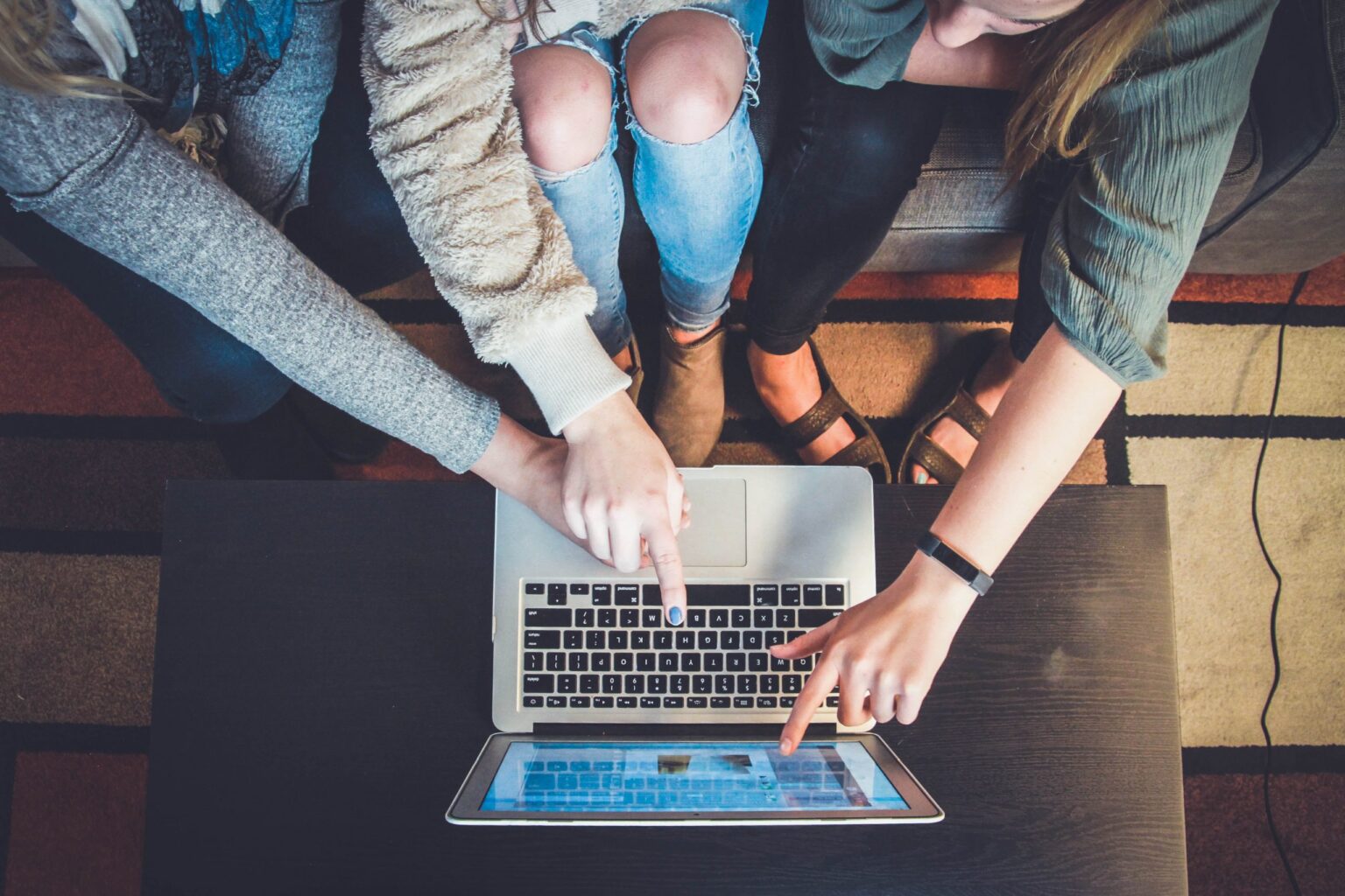 Drei Personen sitzen auf einer Couch vor einem Laptop und zeigen mit ihren Fingern auf den Bildschirm des Laptops.