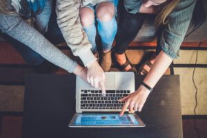 Drei Personen sitzen auf einer Couch vor einem Laptop und zeigen mit ihren Fingern auf den Bildschirm des Laptops.